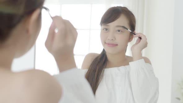 Beautiful young asian woman applying makeup eyebrows brush.