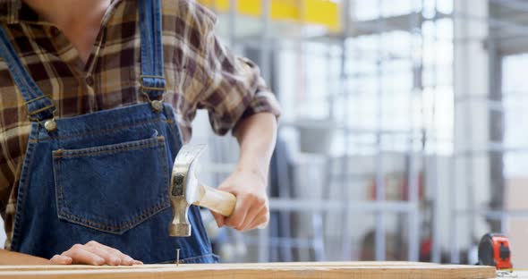 Female welder hammering nail on a wooden plank 4k