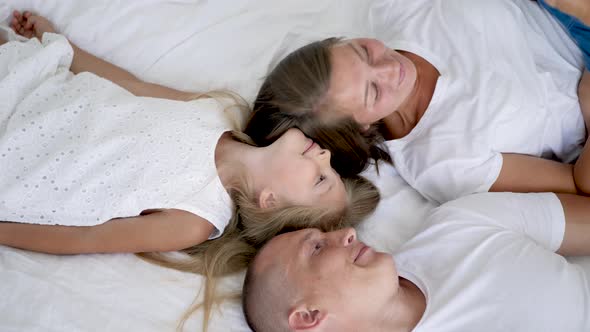 Family with Two Children Lie on a White Big Bed