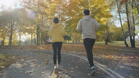 Man and Woman Running on a Track at the City Park in Sunny Autumn Morning