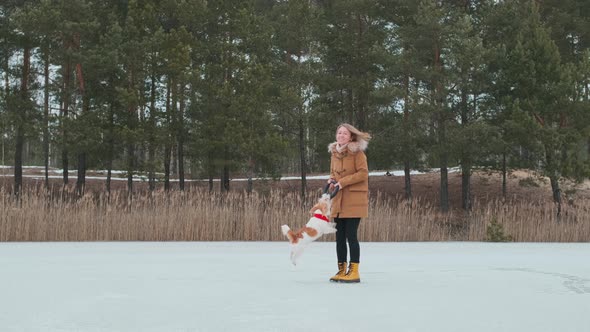 A girl in a coat and yellow boots plays in the winter on the ice of the lake with a dog