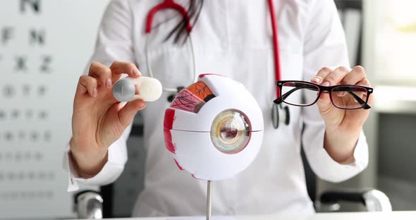 Doctor Ophthalmologist Holding Container with Contact Lenses and Glasses in Front of Artificial