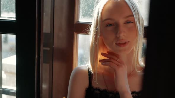 fashion portrait of a beautiful young woman with blue eyes and blonde hair poses near the window