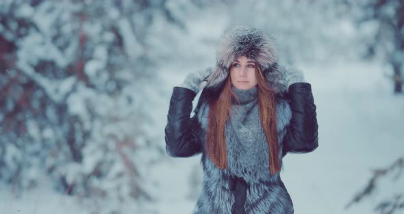 Beautiful Girl in a Fur Hat and Jacket Walks in the Park in Winter