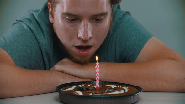 A Man Is Blowing Out a Candle on a Birthday Cake