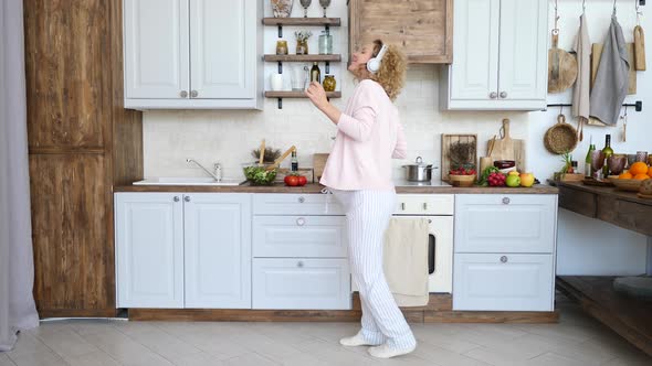 Happy Healthy Pregnancy Concept. Pregnant Woman Dancing On Kitchen With Smartphone.