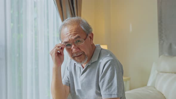 Portrait of Happy Asian Senior elderly grandfather sit on sofa at home put eyeglasses on his face.