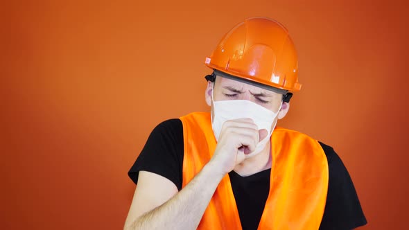 Male Construction Worker in Overalls and Medical Mask Coughing on Orange Background