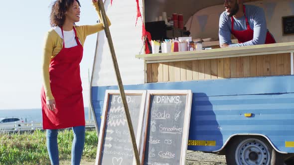 Portrait of african american couple wearing aprons smiling while standing near the food truck