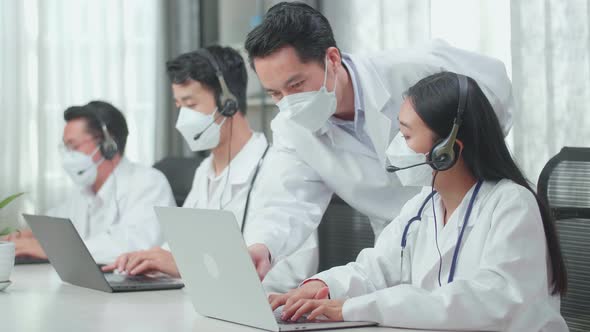 A Man Coming To Help A Woman Of Three Asian Doctors In Masks Working As Call Centre Agent