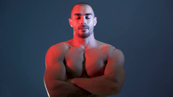 Fitness Model with Arm Tattoo Crosses Arms in Front of Chests and Poses in Studio Shirtless