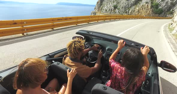 Friends having fun driving on the road along the coast in red convertible