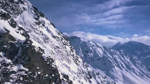 Aerial drone shot of dramatic mountain cliffs and snow covered alps into the distance above the ski