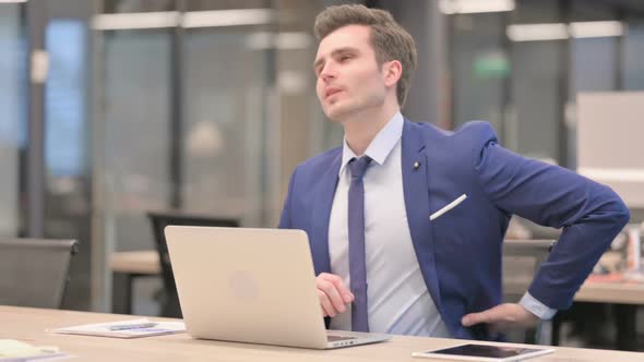 Businessman Having Back Pain While Using Laptop in Office
