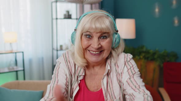 Overjoyed Senior Woman in Wireless Headphones Dancing Singing on Cozy Couch in Living Room at Home