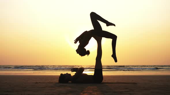 Fit Sporty Couple Practicing Acro Yoga with Partner Together on the Sandy Beach