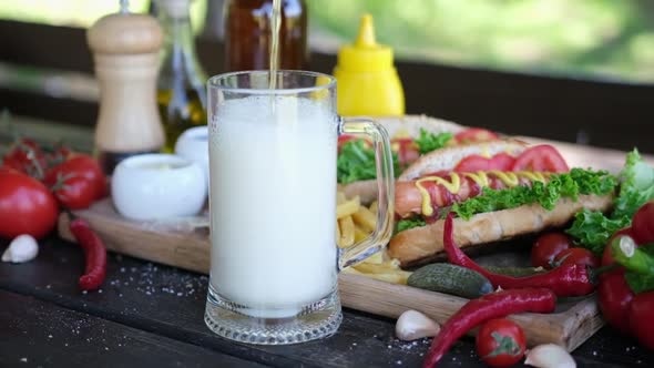 Beer Glass Mug and Freshly Made Grilled Hotdogs and French Fries on a Wooden Board