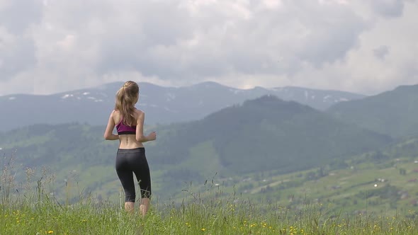 Young woman tourist raising her hands in yoga gestion while hiking in summer mountains.