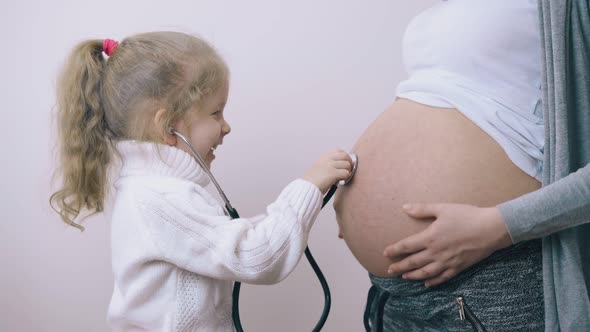 Cute Girl Puts Stethoscope To Pregnant Mother Tummy at Wall