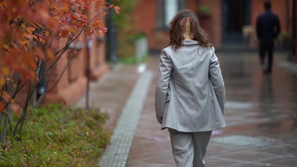 a Middleaged Woman with an Orthopedic Collar Around Her Neck and a Gray Suit Walks Down a Damp