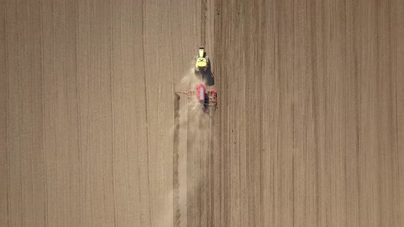 Top down aerial view of green tractor cultivating ground and seeding a dry field. Farmer preparing 