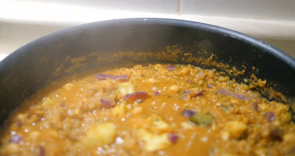 Close up shot of Indian dal (lentil) been cooked in a black pan with cauliflower, chickpeas, onions
