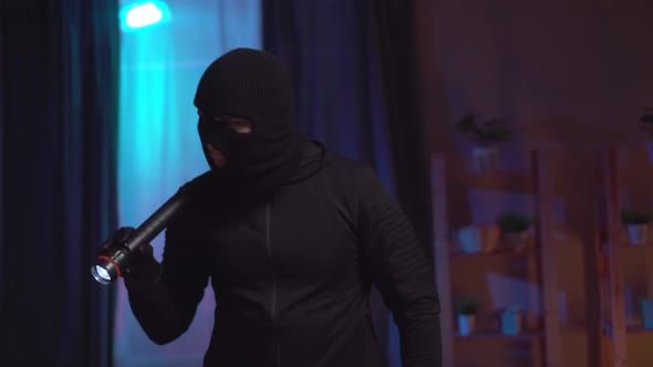 Portrait of a Robber in a Balaclava with a Flashlight in the Apartment