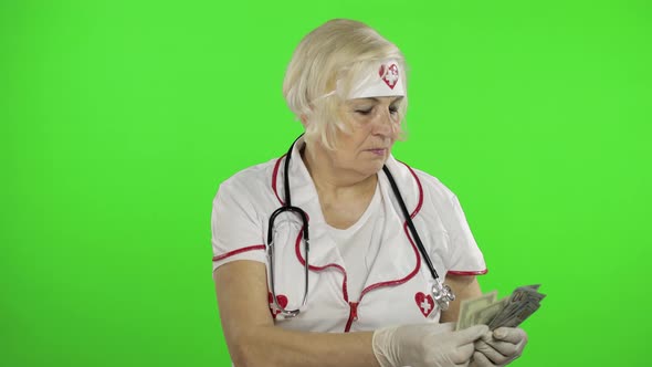Elderly Caucasian Female Doctor Receives Money. Concept of Corruption alt