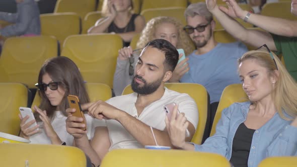 Relaxed Men and Women of Different Ethnicities Sitting with Smartphones in Cinema. Group of People