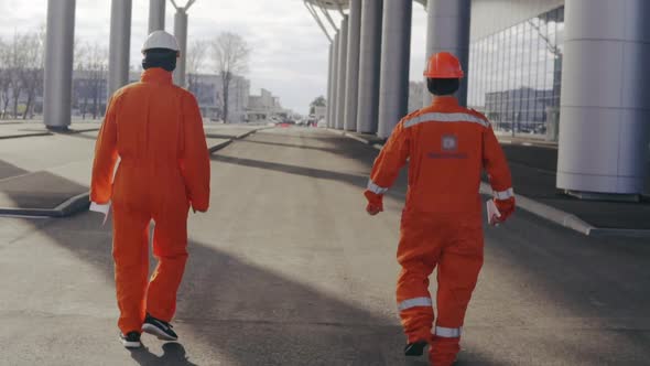 Two Happy Construction Workers in Orange Uniform and Helmets Walking and Jumping Together