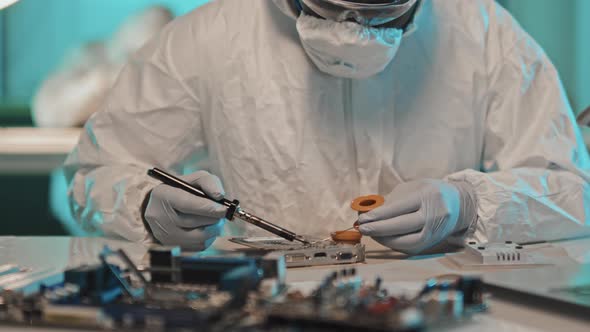 Engineer in Protective Uniform Working with Soldering Iron in Lab