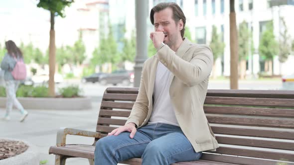 Young Man Coughing While Sitting on Bench