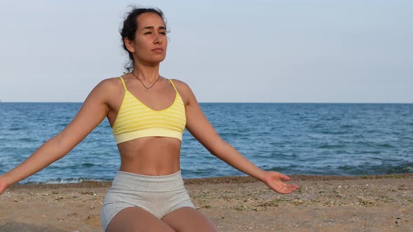 Beautiful tanned young woman sitting in a meditation pose on the beach, lotus position, medicine