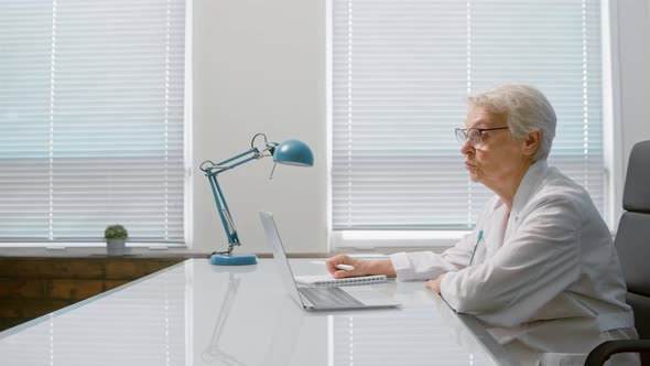 Grey haired senior woman doctor with glasses talks to patient