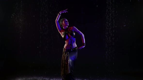 A Woman Who Dances an Oriental Dance on a Black Background in the Pouring Rain