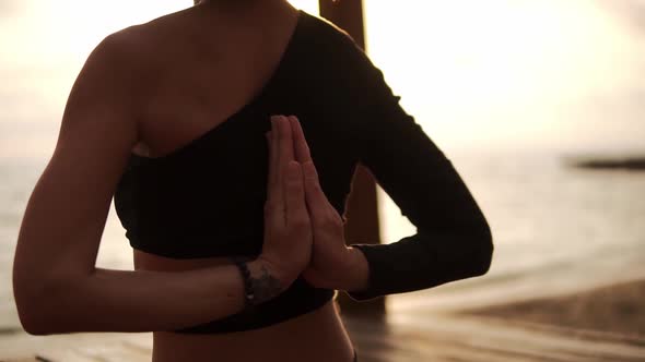 Woman Practicing Yoga and Stretching Spine and Hands Sitting on Mat on Sea Pier Joins Hands Behind