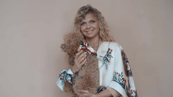 Beautiful Smiling Girl with a Poodle Dog in Her Hands and a Scarf Posing at Camera
