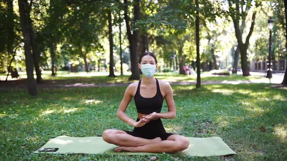 Athletic Young Woman in a Medical Protective Mask Doing Yoga in the Park