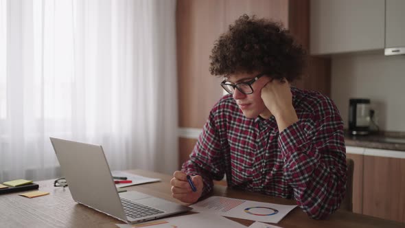 Brooding Serious Curly Freelancer Man Sit at Table in Comfortable Home Office Room Work on Laptop