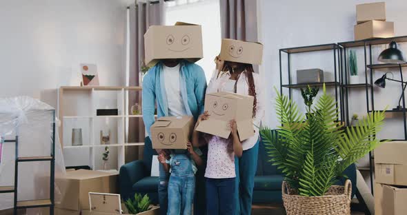 Modern Family with Two Small Kids Hiding their Heads Under Carton Boxes with Depicted Smiles