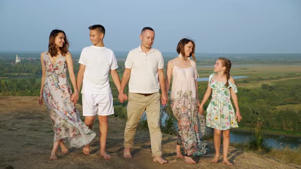 Family with Children Walks Joining Hands Along Riverbank