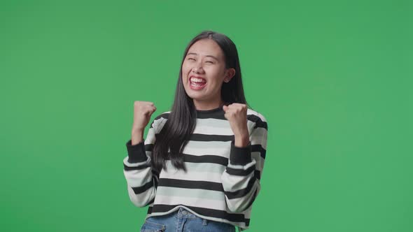 A Happy Asian Woman Celebrating While Standing In Front Of Green Screen Background