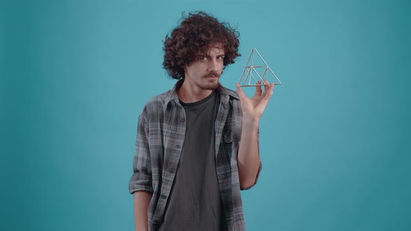 The Charismatic Young Man Holds an Iron Pyramid in His Hand Spins It and Looks at It Curiously