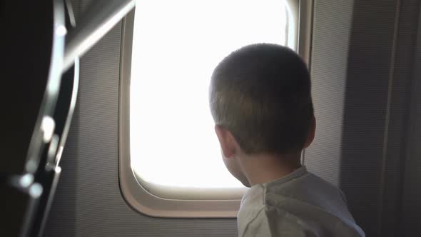 Young Cute Boy Sitting on the Seat and Opens Up Airplane Window