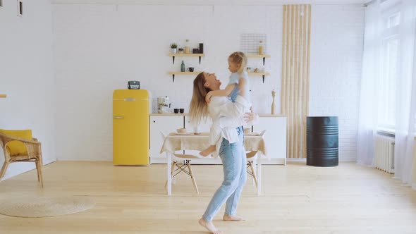 Young Modern Mother with Little Daughter Having Fun Tossing Kid Holding