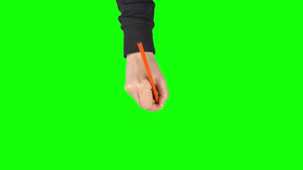 Female Hand in a Black Sweater with Orange Pencil Is Writing on Green Screen Background. Close Up