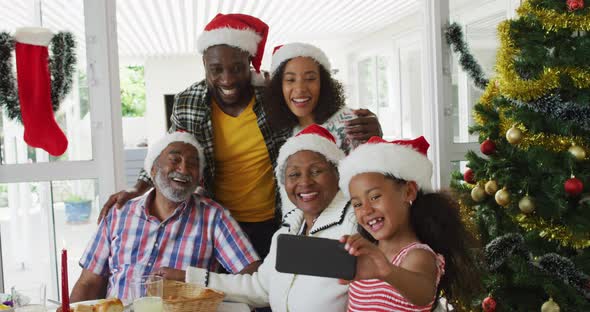 Happy african american multi generation family wearing santa hats, taking holiday selfie