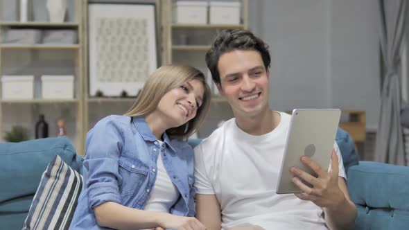 Online Video Chat on Tablet By Young Couple Sitting on Couch