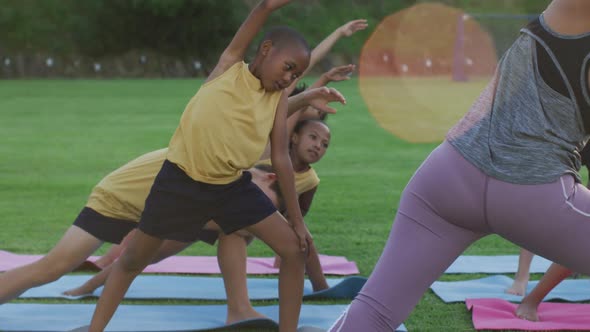 Mixed race female teacher showing diverse group of schoolchildren yoga stretching exercises outdoors