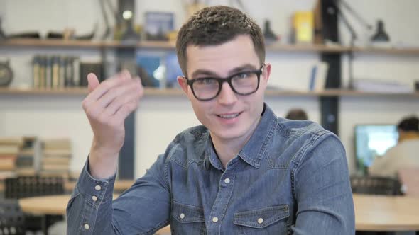 Inviting Gesture By Creative Young Man in Glasses at Work